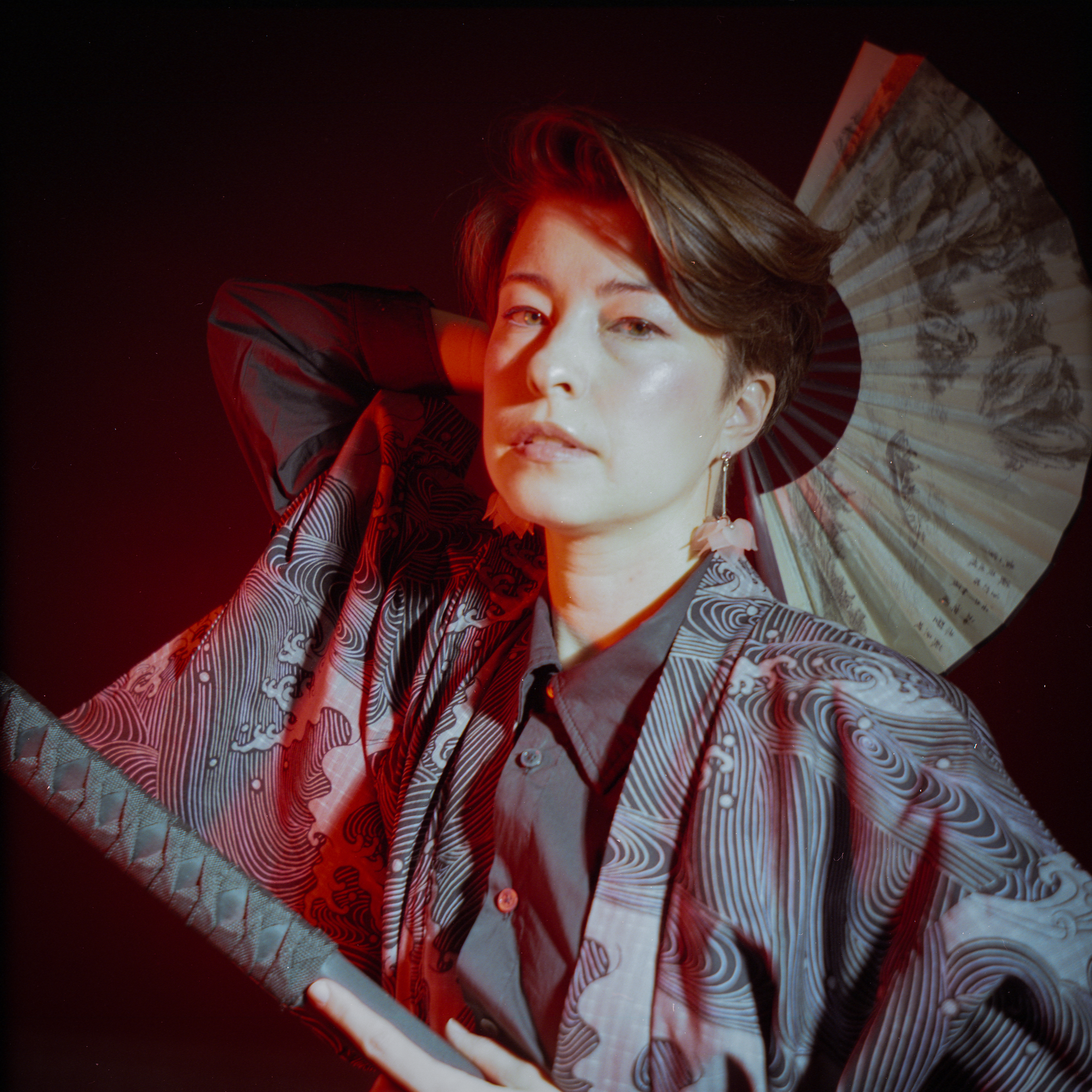 Yulia in red light with a paper fan and katana — close portrait